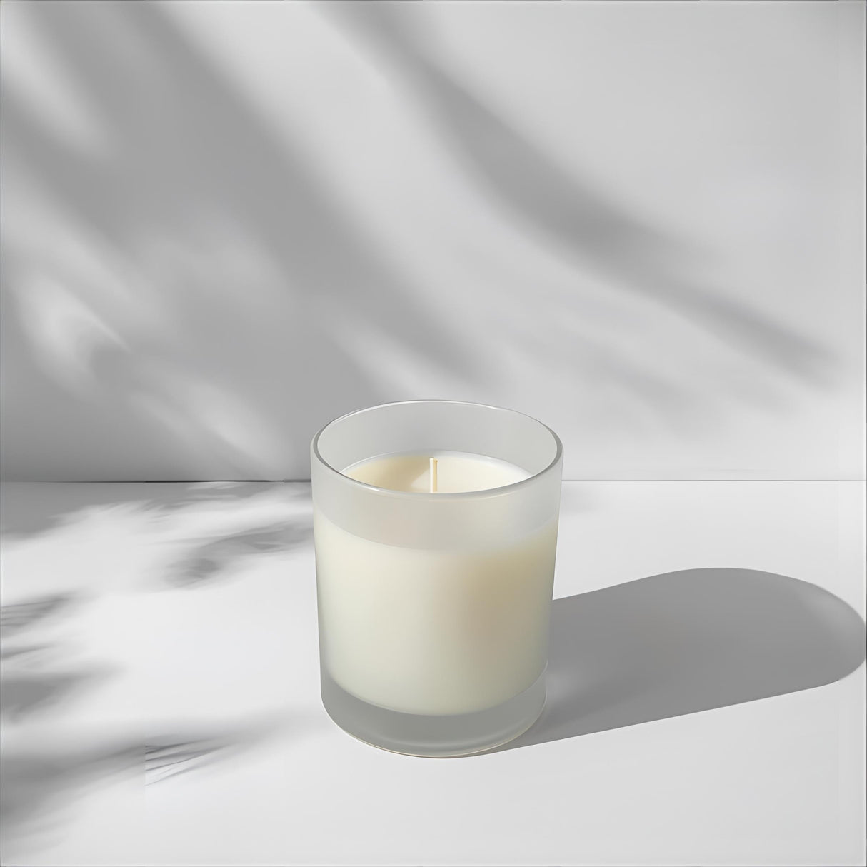 White candle in a glass holder on a light gray surface with soft shadows