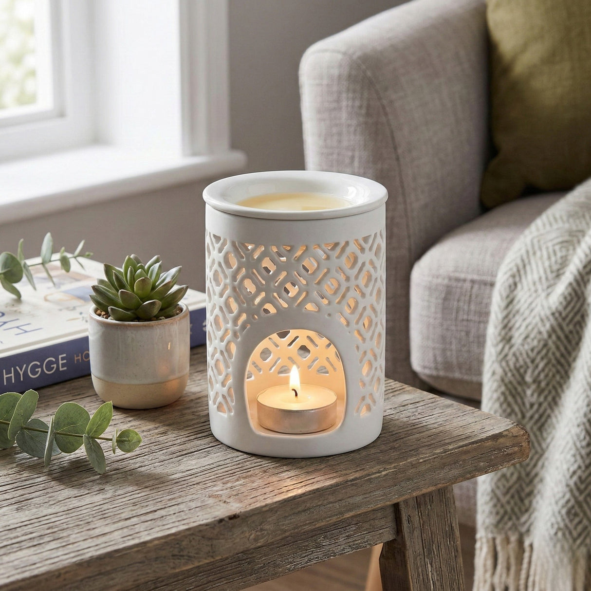 White lace-patterned candle holder with a lit candle on a wooden table in a cozy living room.