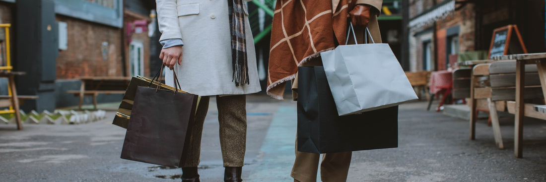 Two women wrapped up in coats and scarves holding shopping bags. Sourced from Pexels.