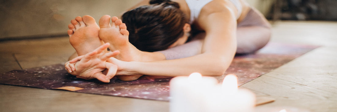 Woman in athletic clothing stretching on a yoga mat with two candles beside her. Sourced from Pexels.