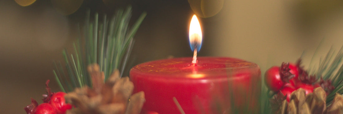 Bright red candle surrounded by pine cones, red berries and pine. Sourced from Pexels.
