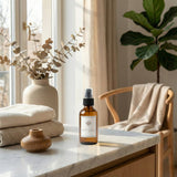 A bottle of essential oil spray on a marble surface with decorative items and a plant in the background.