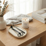 Candle with a brand logo on a wooden surface with a tray and scissors.