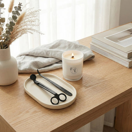 Candle with a brand logo on a wooden surface with a tray and scissors.