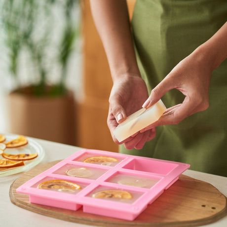 Person using a pink silicone mold to make soap on a wooden board with a blurred background