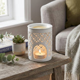 White lace-patterned candle holder with a lit candle on a wooden table in a cozy living room.