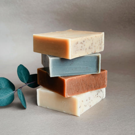 Stack of five different colored soap bars on a neutral background with a leaf.