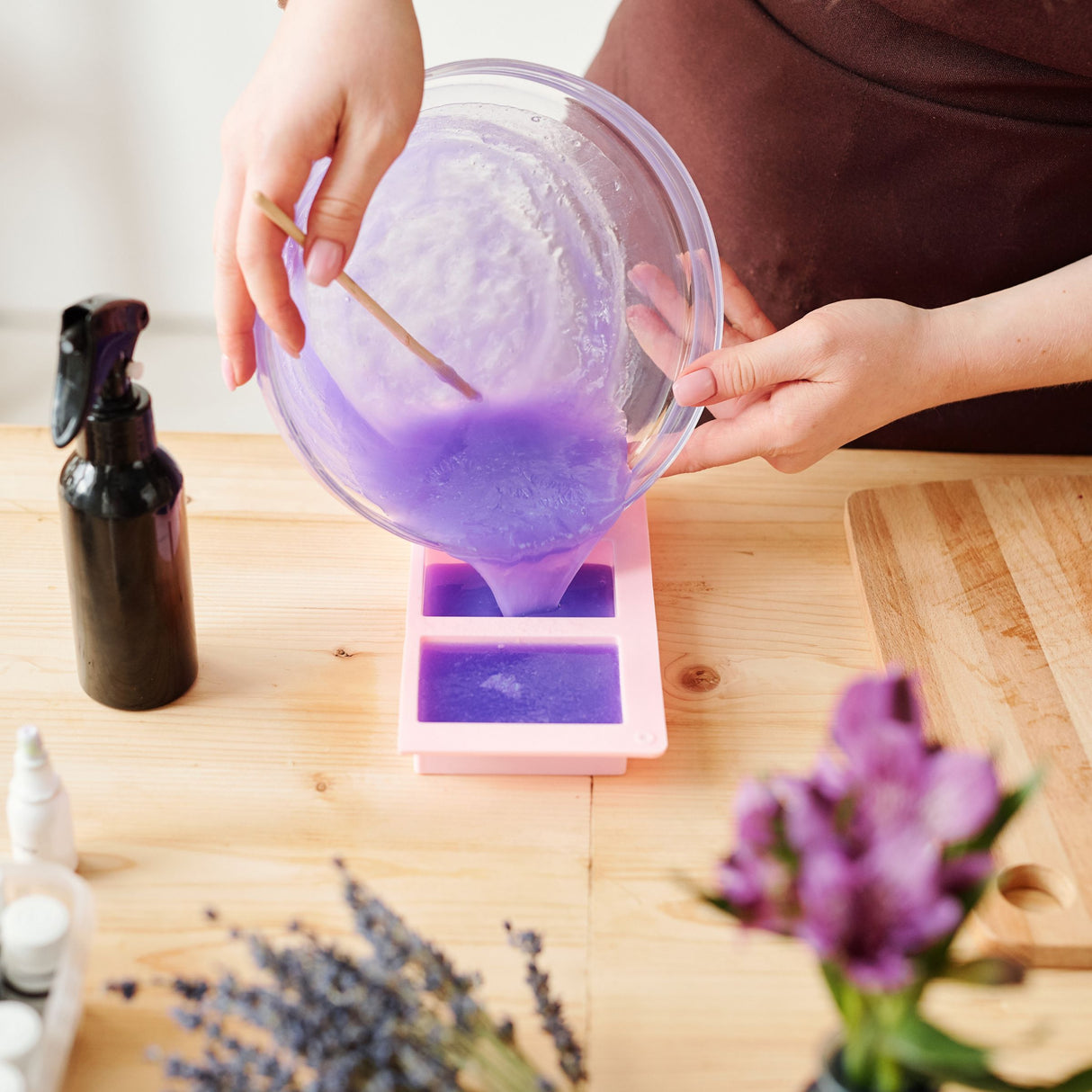 Person pouring purple liquid into a mold on a wooden table with lavender flowers.